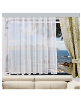 Ein Wohnzimmerfenster ist mit durchsichtigen weißen Vorhängen und einem zur Seite gezogenen geblümten Vorhang verhängt. Der Blick durch das Fenster zeigt ein ruhiges Meer, eine felsige Küste und ferne Berge. Im Vordergrund ist ein Teil eines beigen Sofas zu sehen.