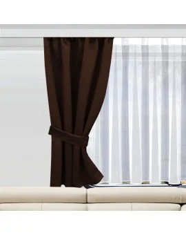 Ein brauner Vorhang, der an einer Seite zusammengebunden ist, verdeckt teilweise ein Fenster, hinter dem sich ein durchsichtiger weißer Vorhang befindet. Das Fenster befindet sich über einem hellen Sofa. Natürliches Licht fällt durch den durchsichtigen Vorhang und erhellt den Raum.