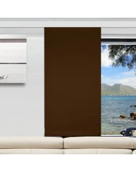Ein moderner Camperraum mit einer weißen Couch, einem braunen vertikalen Flächenvorhang, der ein Fenster teilweise verdeckt, und Wandkunst auf der linken Seite. Der unbedeckte Teil des Fensters zeigt Berge, blaues Meer und Felsen in der Aussicht nach draußen.