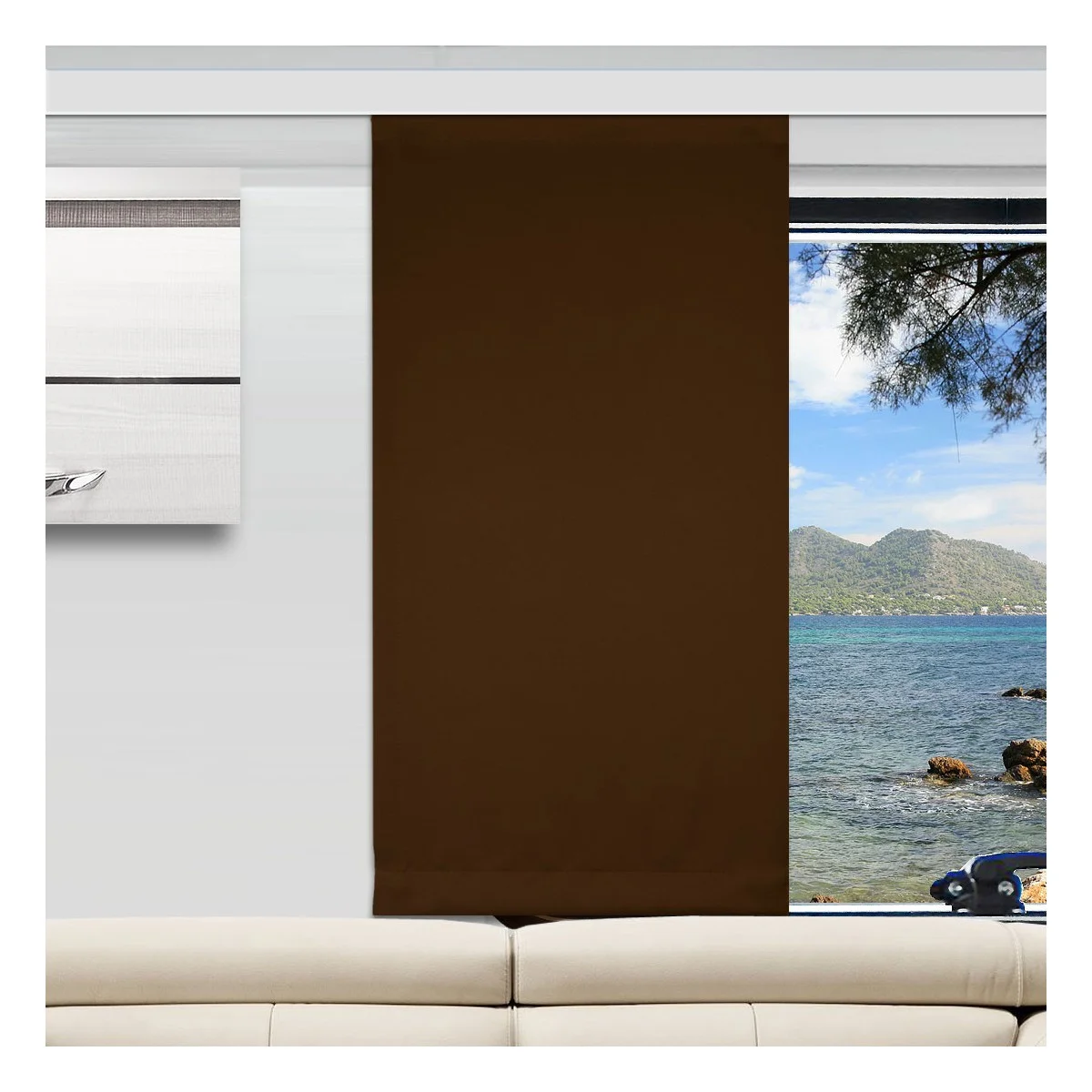 Ein moderner Camperraum mit einer weißen Couch, einem braunen vertikalen Flächenvorhang, der ein Fenster teilweise verdeckt, und Wandkunst auf der linken Seite. Der unbedeckte Teil des Fensters zeigt Berge, blaues Meer und Felsen in der Aussicht nach draußen.